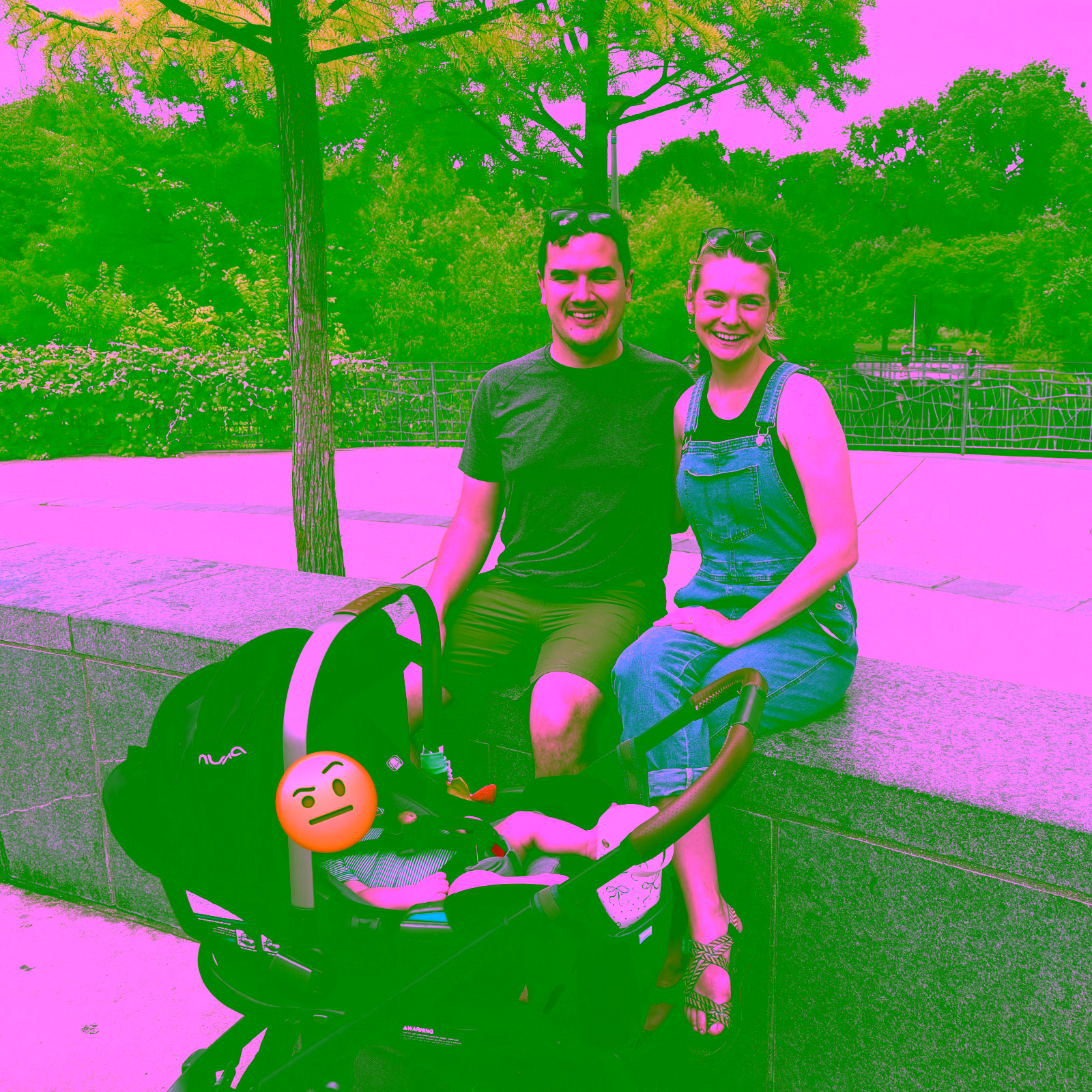 A young couple sitting on a barrier with a newborn baby in a stroller in front of them